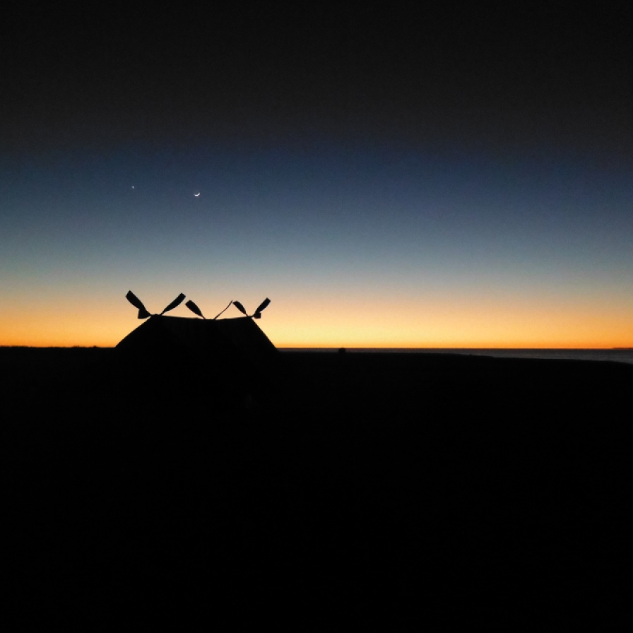 The sun just rising on the horizon, the moon and a single star hovering above the makeshift tent we built on the desert island.